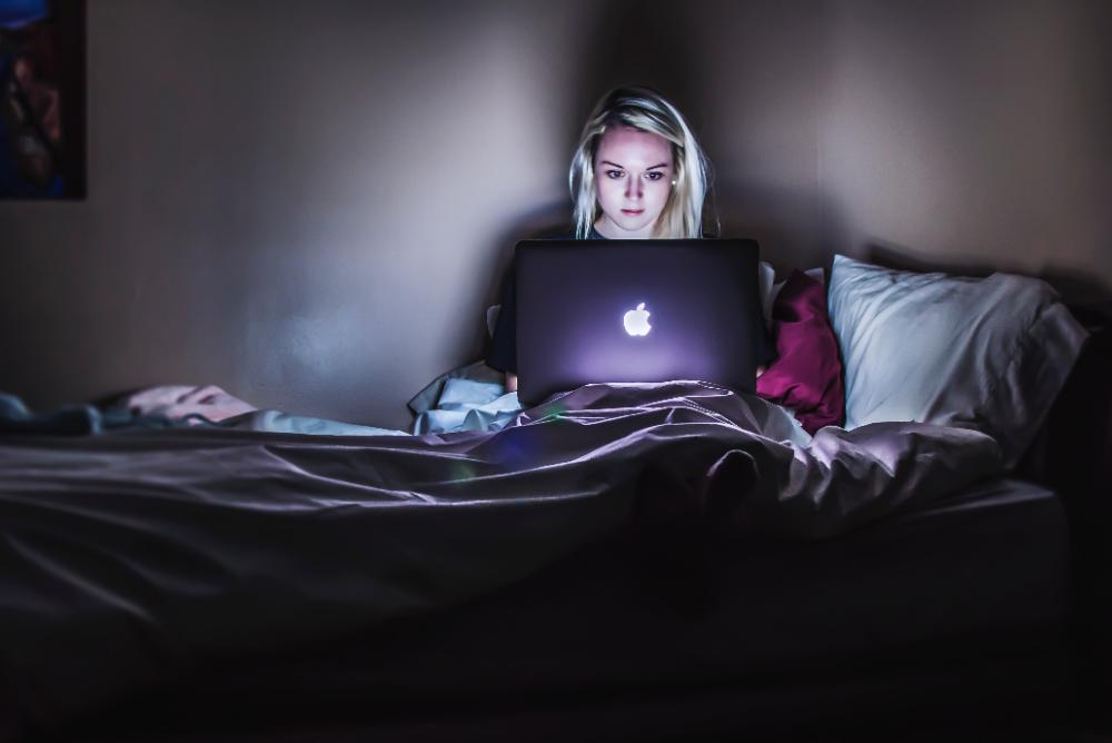 woman on bed in dark with laptop