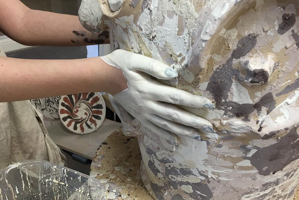 Clay-covered hands shape a ceramic pot in progress.