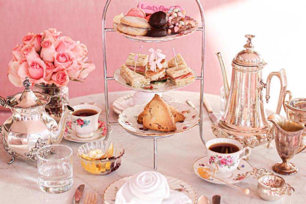 Image of a tea table with teacups, baked goods, and flowers.
