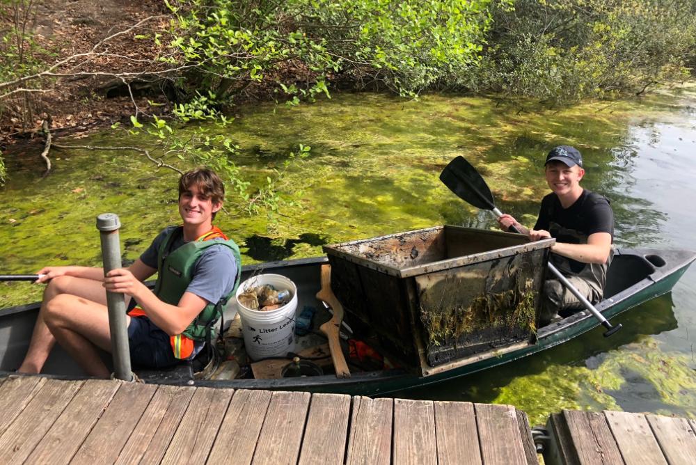 Two students in a canoe with trash they have collected