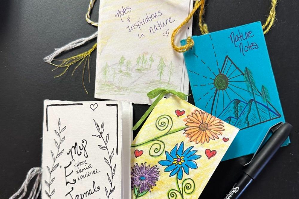 Image depicts four handmade journals and a pen atop a black table