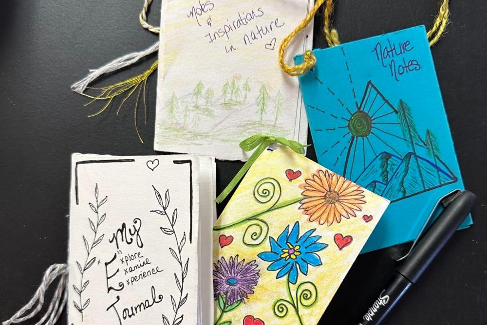 Image depicts four handmade journals and a pen atop a black table