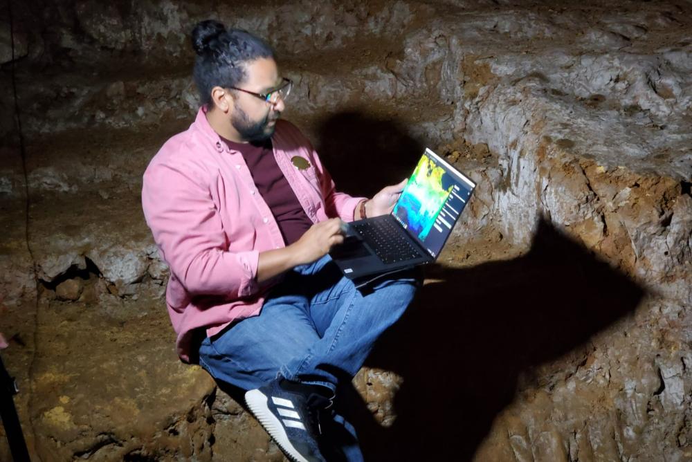 Scientist in a cave, holding laptop with data visualization on the screen