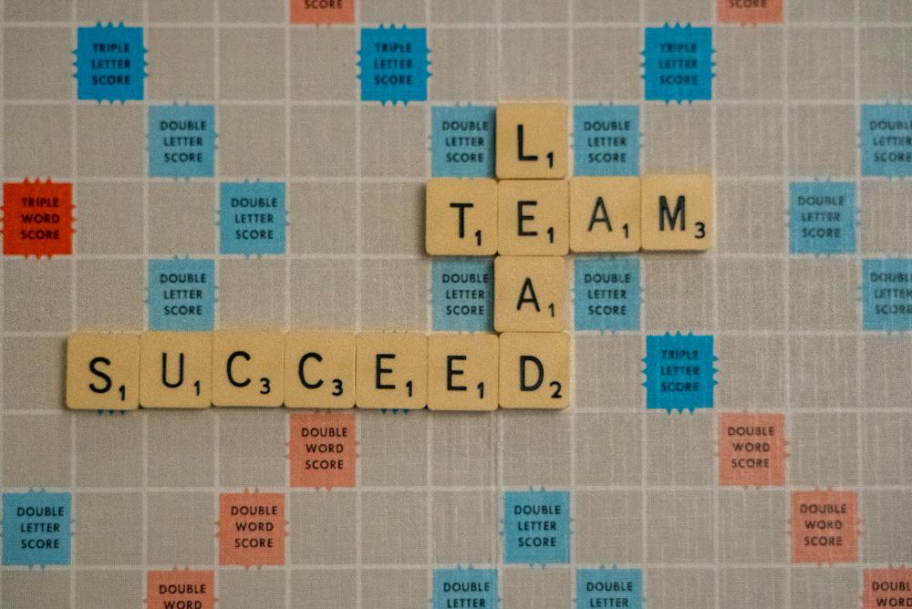 Scrabble tiles that interconnect to spell lead, team, succeed